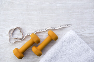 Orange weights, measure meter and towel on wooden table, sport, fitness time