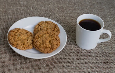 Cookies on a white plate and mug with coffee. Background of burlap