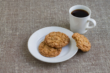Cookies on a white plate and mug with coffee. Background of burlap