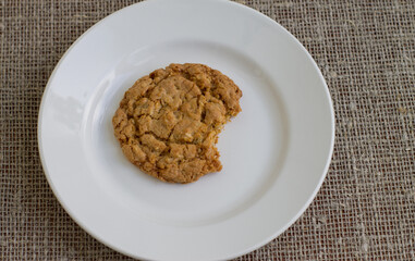 A bitten cookie on a white plate. Background burlap