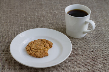 Bitten a cookie on a white plate and a mug of coffee. Background burlap