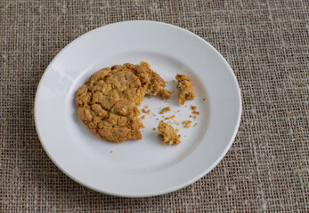 A bitten cookie on a white plate. Background burlap