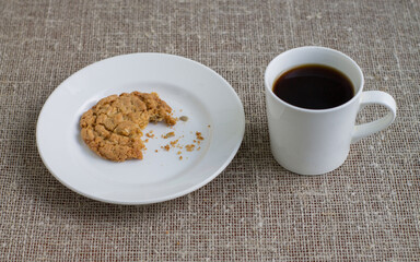 Bitten a cookie on a white plate and a mug of coffee. Background burlap