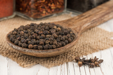 Black peppercorns in a wooden spoon and old wooden table.