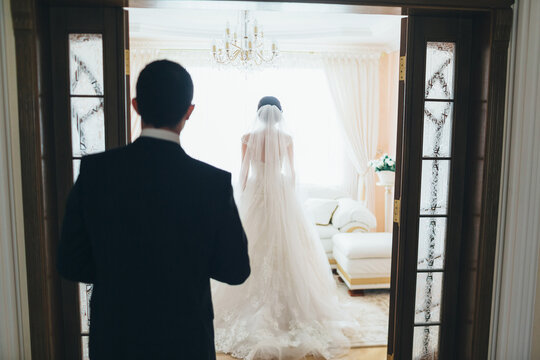 The bride stands in the room and groom looking at his bride