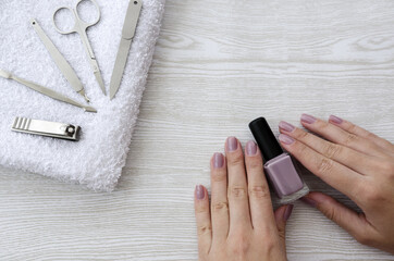 Female hands with purple nail polish on wooden table with towel and nail set