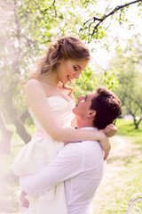 Fototapeta premium bride and groom with a bouquet of red peonies in the summer standing in a field with blooming apple trees