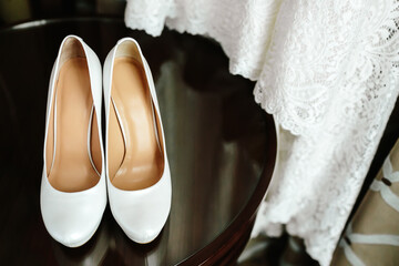 Elegant stylish white wedding shoes on wooden table with a dress in background