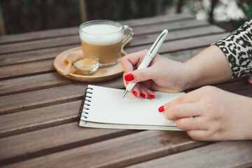 Woman's hands writing on notebook , hot coffee and vintage wooden table background