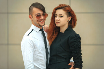 Couple in love. Handsome guy in sunglasses and pretty girl posing opposite modern urban background.