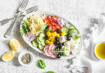 Greek lemon orzo salad. Feta, orzo, tomatoes, cucumbers, radishes, olives, peppers salad on a light background, top view. Healthy food concept. Mediterranean food style