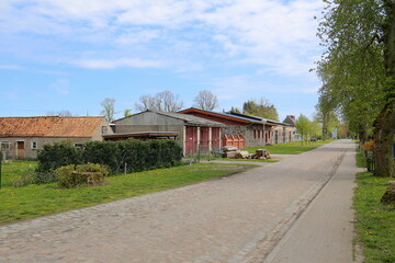 Fototapeta na wymiar Cobblestone street with buildings belonging to the manor grounds in Behrenhoff, listed as monument