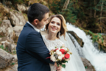 Hugging wedding couple stands before a waterfall