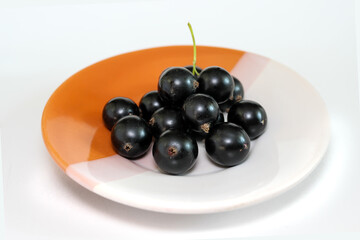 Large shiny black currant berries on a plate.