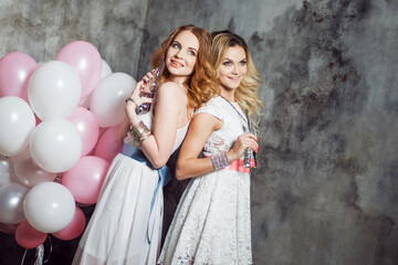 Blonde and redhead. Two young charming girlfriends at the party with balloons. On gray textured background