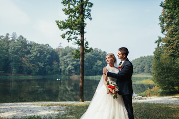 Groom hugs bride tender posing on the shore of a lake