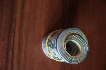 A lot of money on a wooden background.  US dollars on one banknote, scattered, with a rubber band