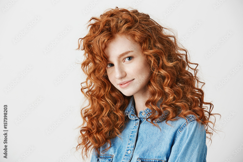 Wall mural Portrait of pretty redhead girl smiling looking at camera over white background.