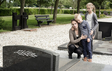 Young widow visiting graveyard with kids