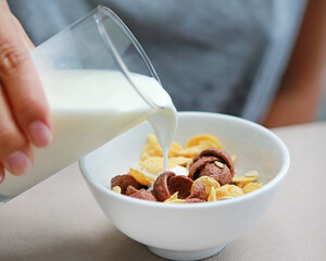 milk pouring into bowl of muesli on table.