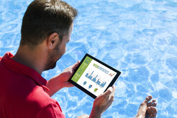 Man consulting web statistics with a tablet while sitting in the swimming pool edge.
