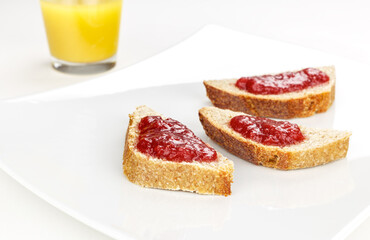 red fruit marmalade on sliced bread on white serving plate and orange juice glass