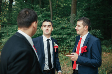 Cheerful groom and groomsmen talk in the forest