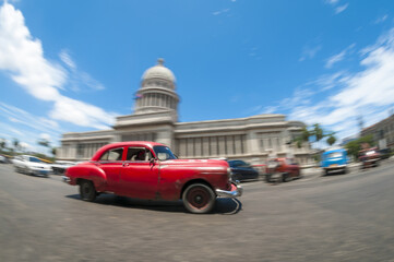 Brightly colored classic American cars serving as taxis pass on the main street in front of the...