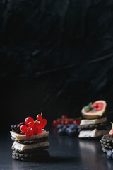 Black charcoal crackers with camembert brie cheese and berries blueberry, dewberry, red currant and sliced figs, served on vintage tray over dark metal background. Summer appetizer