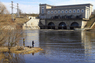 people are fishing on river Narva against the background of hydroelectric power station