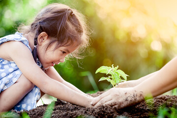 Asian little girl and parent planting young tree on black soil together as save world concept in...