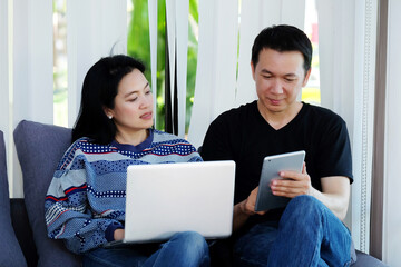 Fototapeta premium The couple using lab-top computer and tablet sitting on sofa at home, lifestyle, internet of things concept