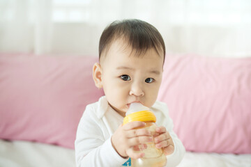 Sweet baby girl sucking milk in bottle at home.