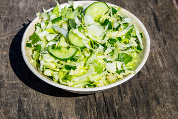 Spring vegan salad with cabbage, cucumber, green onion and parsley on wooden table