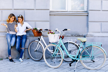 Fototapeta premium Two young women with bikes using smartphone