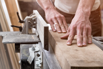 The joiner aligns the board on the electric plane. Preparation of a wooden timber for work