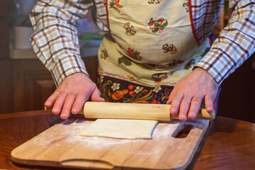 An elderly man in an apron rolls dough on a board