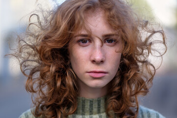 Beautiful red-haired girl with long curly hair gently looking at the camera. People and lifestyle concept