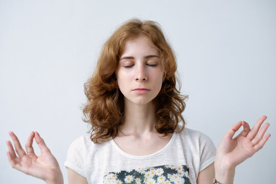 Girl with red hair holding fingers together. Eyes closed. Meditate or make a wish, trying to calm down.
