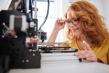Nice pleasant woman looking at the 3d printer details