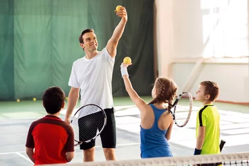 Foto op Canvas Cheerful trainer teaching kids playing tennis © Yakobchuk Olena