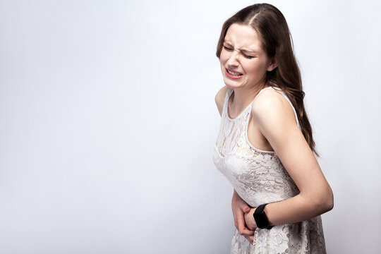 Portrait of beautiful woman with freckles and white dress and smart watch with stomach pain on silver gray background. healthcare and medicine concept.