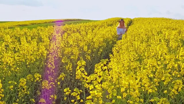 Happy woman with long hair walks on yellow field full of flower