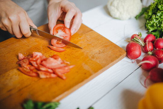 Woman hands cutting fresh red tomato on wooden board closeup. White table background.