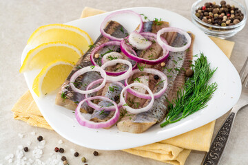 Marinated herring fillets with red onion, dill and spices on white plate.