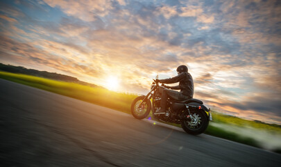 Obraz na płótnie Canvas Dark motorbiker riding high power motorbike in sunset