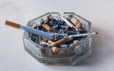 A cigarette with a filter in a dirty ashtray with cigarette butts, conceptual photography,