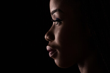 Side view portrait of dark skinned model on a black backstage. Light and shadow portrait of a woman...