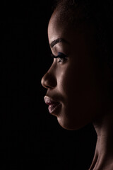 Dark skinned model on a side view portrait. Close up view of a model on black backstage.