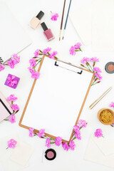 Blogger or freelancer workspace desk with clipboard, notebook, pink flowers and accessories on white background. Beauty blog concept. Flat lay, top view.